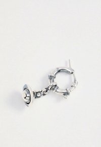 Boucle d'oreille anneau en argent avec plusieurs bandes enroulées et un petit pendentif suspendu en forme de planète avec des anneaux sur un fond blanc.