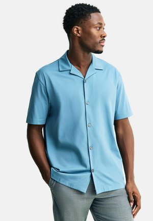 Hellblaues Kurzarm-Hemd mit Kamp-Kragen, glatter Textur und schwarzen Knöpfen, kombiniert mit grauer Hose.