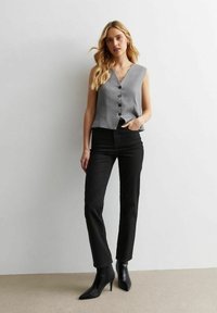 Top gris sin mangas con escote en V y botones negros, combinado con pantalones ajustados negros y botas de tacón alto puntiagudas. Tela suave, corte a medida.