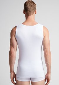 Hvid bomulds tanktop med rund halsudskæring, der viser et tætsiddende design og ribbet tekstur, set bagfra på en neutral baggrund.
