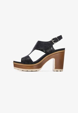 Sandalia de tacón con tira trasera de piel negra perforada, plataforma marrón y tacón grueso, con hebilla ajustable y suela texturizada.