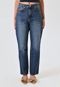 Jeans in denim blu a vita alta con taglio dritto, caratterizzati da un leggero sbiadimento e un classico design a cinque tasche.