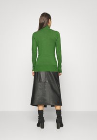 Vihreä neulottu pooloneule yhdistetty mustaan nahkaiseen midihameeseen. Asussa on istuvat hihat ja resorireuna. Mukana mustat nilkkurit.