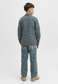 Karirana flanel srajca v temno modri in beli barvi, dolgi rokavi, ostri ovratnik, kombinirana s svetlo modrimi širokimi kavbojkami in bež obutvijo.