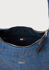 Bolsa de ombro em denim com um padrão em relevo "tommy jeans" em laranja. Apresenta um fecho com zíper e um interior em azul-marinho com um rótulo de marca.