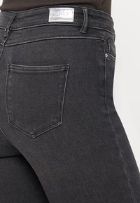 Čierne džíny z denimu s priliehavým strihom, s zadnou vreckom, prešitými detailami a striebornou štítkou na páse.