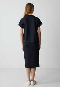 Maglietta nera a maglia con maniche corte, abbinata a una gonna nera al ginocchio. Indossata con sneakers bianche, texture liscia, design minimal.