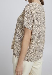 Kortärmad topp i lätt tyg, med ett beige och brunt prickigt mönster. Avslappnad passform med rundad halsringning och sidofickor.