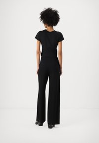 Black T-shirt with short sleeves paired with high-waisted, wide-leg trousers. Smooth fabric, minimalist design, and no visible patterns or accents.