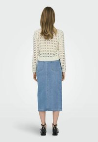 Gehaakte crèmekleurige sweater met open structuur, gecombineerd met een lichtblauwe denim midi-rok met achterzakken, gedragen met zwarte enkellaarsjes.