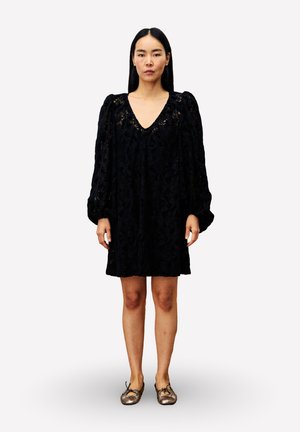 Robe en dentelle noire à motifs floraux avec un col en V et des manches bouffantes, présentant une coupe décontractée, associée à des ballerines métalliques.