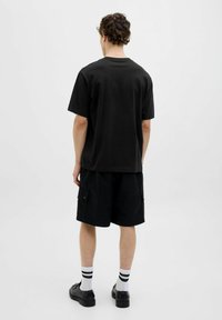 Zwarte katoenen t-shirt met korte mouwen, gecombineerd met zwarte cargoshorts. De outfit bevat zwart-wit gestreepte sokken en zwarte schoenen.