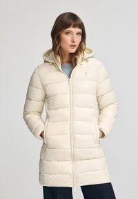 Opvaskjakke i lys creme med hætte, der har lynlås lukning, ribbede manchetter og lodrette baffel-syninger. Minimalistisk design med logo detalje.