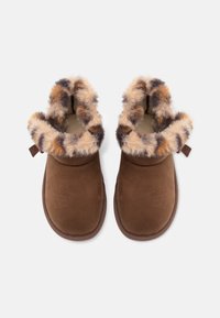 Des chaussons marron en matériau doux semblable au daim, avec un manchon en fourrure moelleux et multicolore. L'intérieur est doublé pour plus de chaleur et de confort.