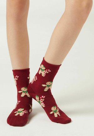 Vinrøde ankelsokker med peberkagemandomønster, grønne accenter og slikstokke, lavet af et blødt, elastisk stof.