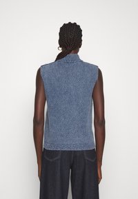 Jersey de denin sin mangas con un diseño de canalé texturizado, color azul claro, cuello alto y cintura ajustada. Vista trasera que muestra el detalle de los hombros.