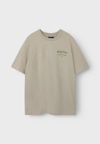 Beige t-shirt met korte mouwen van zachte katoen, met een groene opdruk van "Shady Pines Golf Club." Ronde halslijn en een relaxte pasvorm.