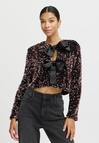 Kraftigt black sequin-jakke med rosa accenter, der har to store sorte satin-sløjfer ved halsen og lange ærmer. Matched med højtaljede jeans.