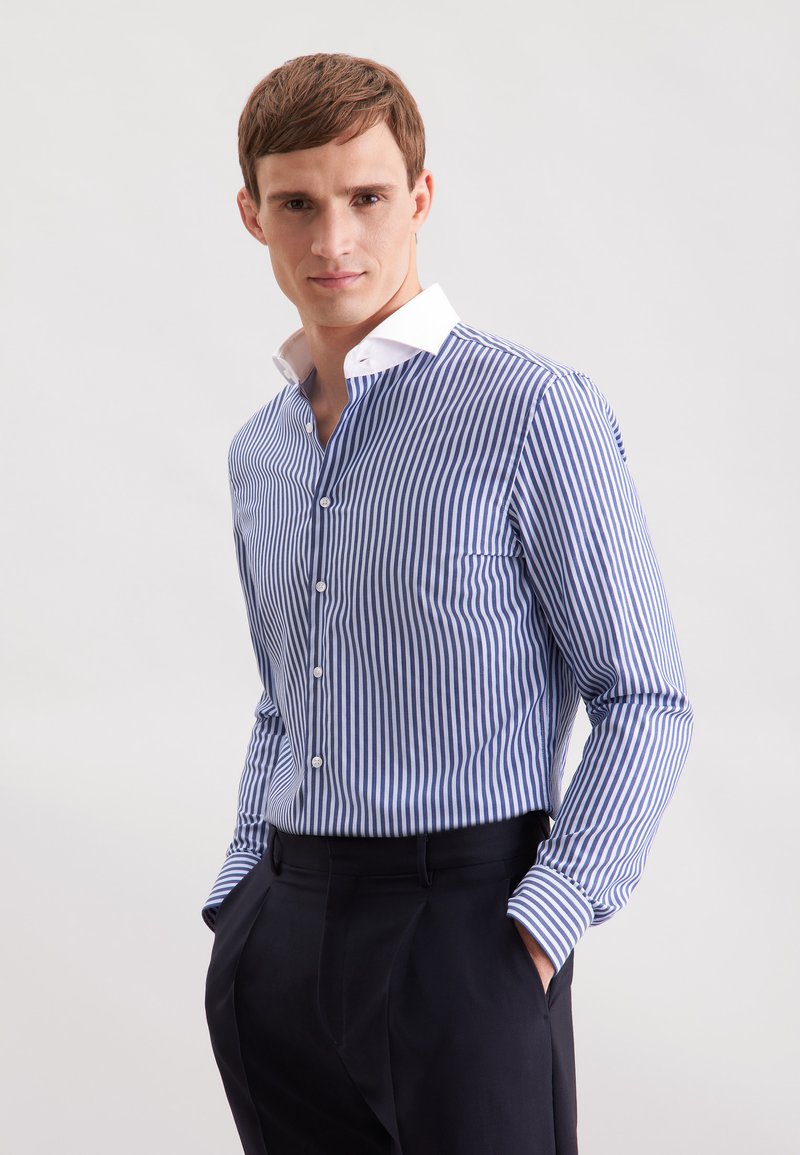 Camicia a righe blu e bianca. Presenta un colletto button-down, taschino frontale e maniche lunghe con polsini abbottonati. Vestibilità tailored.