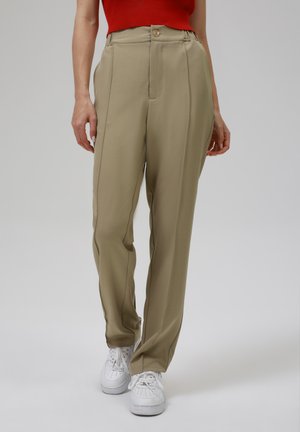 Beige high-waisted broeken met een knoopsluiting, voorzien van verticale naden, een getailleerde pasvorm en gecombineerd met witte sneakers.