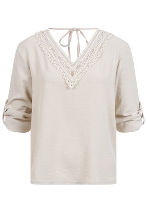Béžová halenka s tříčtvrtečními rukávy stočenými nahoru, výstřihem do V s krajkovou ozdobou a zavazováním vzadu na krku.
