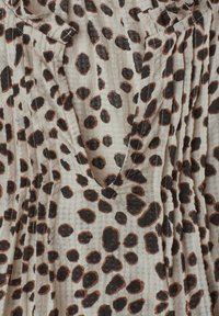 Tissu beige avec des rayures verticales texturées et des taches de léopard brun foncé irrégulières dispersées sur la surface.