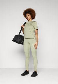 Maglietta atletica verde chiaro e leggings coordinati, con un logo discreto. Una borsa da palestra nera e scarpe da ginnastica nere completano l'outfit.