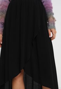 Musta epäsymmetrinen hame, jossa on laskostettu muotoilu, laskeutuva kangas ja korkealaatuiset helmat, yhdistetty gradienteilla neulottuun villapaitaan yläosassa.