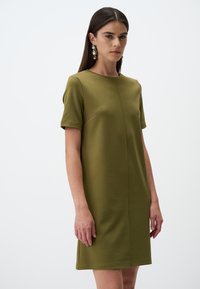 Olivengrünes Kurzarmkleid aus weichem Stoff, mit Rundhalsausschnitt, Seitentasche und gerader Silhouette.