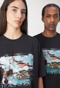 Black cotton t-shirts with a graphic print featuring mythological figures and landscapes, "LEGACY OF ICARUS" text, and contrasting colors.