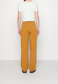 Kortärmad vit t-shirt och senapsgula vida byxor. Byxorna har ett texturerat tyg och bakfickor, kompletterade med bruna skor.