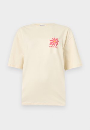 Μπεζ κοντομάνικη μπλούζα με μικρό ροζ λουλούδι και κόκκινο κείμενο "Bliss of Nature" στο αριστερό στήθος.