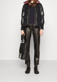 Doudoune noire à finition brillante, doublure colorée à motifs, poignets côtelés. Pantalon en cuir noir, bottines et sac cabas noir.