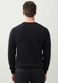 Pulover negru, cu manșon lung, cu un model texturat de tricot, cu manșete și tiv cu nervuri, și guler rotund. Vedere din spate arată cusăturile umerilor.