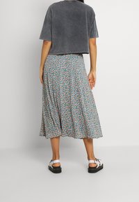 Grå kort t-shirt med korta ärmar, kombinerad med en blå midikjol med blommönster i orange, vitt och grönt. Svarta sandaler.