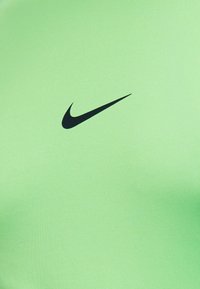Μαύρο λογότυπο Nike Swoosh στο κέντρο ενός λείου υφασμάτινου φόντου σε ανοιχτό πράσινο χρώμα.