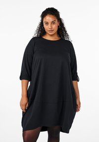 Vestido negro de largo a la rodilla hecho de un tejido suave. Presenta mangas de tres cuartos con detalle de botones y un diseño holgado y relajado.