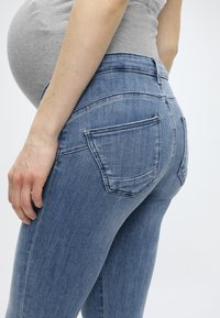 Τζιν εγκυμοσύνης σε μεσαίο μπλε ντένιμ, με εφαρμοστή σχεδίαση, μέση μεσαίας ανόδου και τυπικές πίσω τσέπες. Ομαλή υφή με ελαφριά ελαστικότητα.