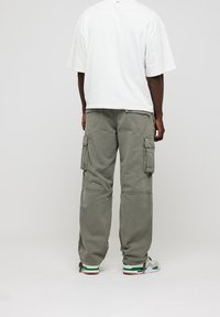 Pantalones cargo de tela verde oliva con dos bolsillos laterales. Corte holgado con piernas rectas. Combinados con una camiseta blanca de corte oversize y zapatillas.