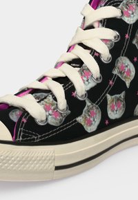 Μαύρο sneaker ψηλής κοπής με λευκά κορδόνια, διακοσμημένο με επαναλαμβανόμενα πρόσωπα γατών που φορούν ροζ γυαλιά ηλίου σε σχήμα αστεριού και ροζ αστροειδή σχέδια.