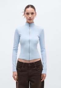 Ανοιχτό μπλε τοπ με φερμουάρ, μακριά μανίκια, ψηλό γιακά, ριμπ υφή και κοντό μήκος, σε συνδυασμό με σκούρο καφέ παντελόνι με ψηλή μέση.