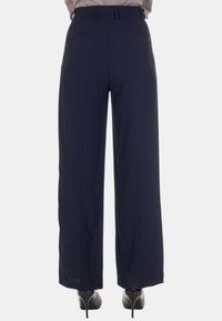 Pantaloni a gamba larga blu navy con una texture del tessuto liscia, due tasche posteriori e una vita sagomata. Indossati con décolleté nere con tacco alto.