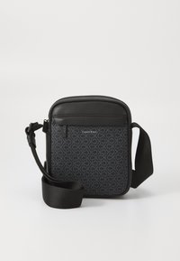Sort crossbody taske lavet af tekstureret materiale, der har et gentagende logo-mønster, lynlåslomme og justerbar rem.
