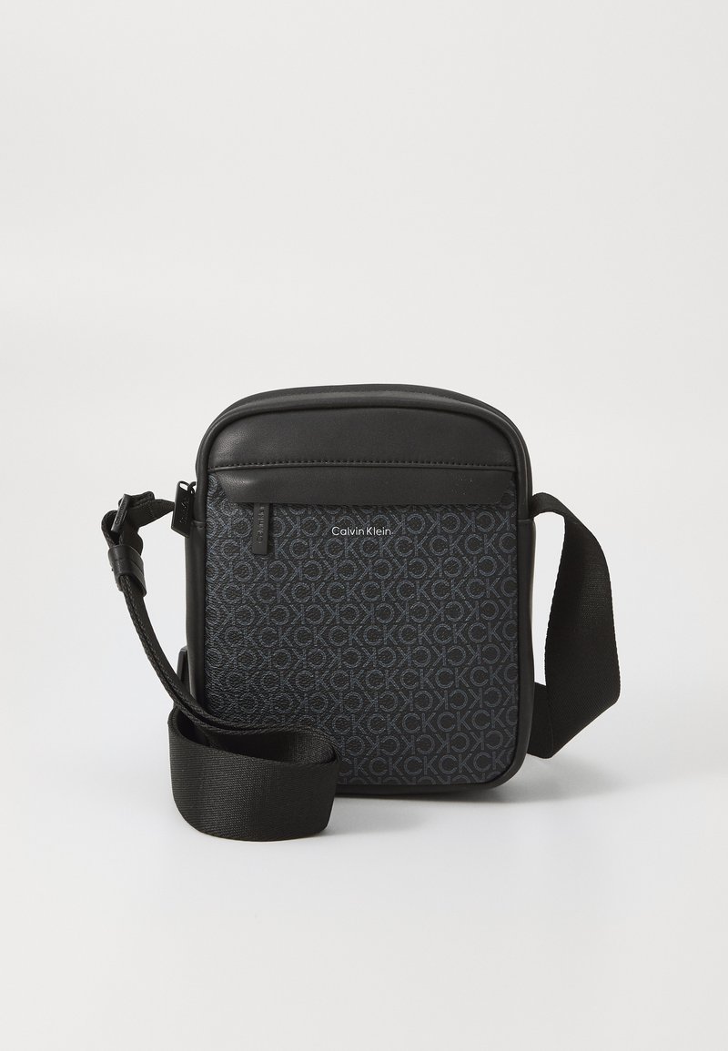 Sort crossbody taske lavet af tekstureret materiale, der har et gentagende logo-mønster, lynlåslomme og justerbar rem.