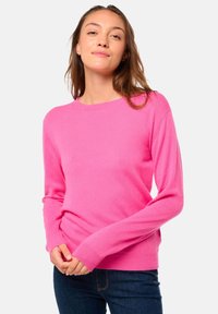 Pull rose en tricot doux, avec des manches longues, un col rond et des poignets côtelés. Porté avec un jean foncé.