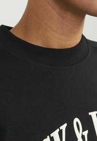 Zwarte sweatshirt met een geribbelde halslijn, gemaakt van textuurstof en voorzien van gedurfde witte grafische letters op de voorkant.