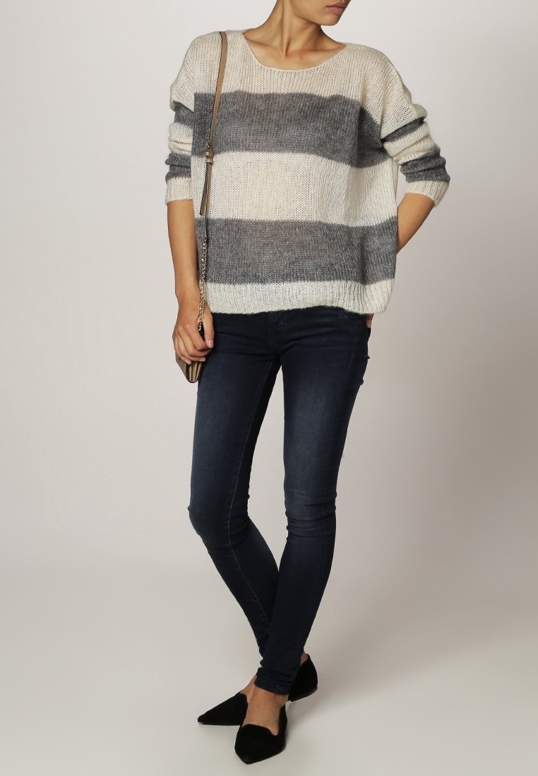 Randig tröja i beige och grå, gjord av stickat tyg, med en avslappnad passform, vid halsringning och trekvartsärmar, kombinerad med mörka jeans.