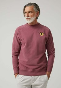 Sudadera burdeos con cuello redondo, puños acanalados y un logo amarillo impreso con alas. Tejido suave y texturizado con un corte relajado.