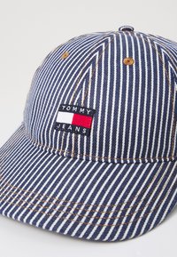 Marineblå og hvide stribede kasket lavet af bomuld med en buet skygge, der har et lille rektangulært Tommy Jeans logo-patch på forsiden.