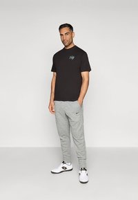 Juoda medvilninė marškinėliai su lengvais pilkais vilnoniais sportiniais kelniukais. Marškinėliai turi turkio spalvos logotipą; kelnės turi Nike logotipą, derinama su baltais sportbačiais.